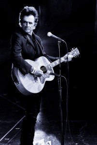 man standing on stage holding a guitar behind a microphone